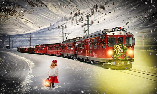 Child standing in snow looking at holiday train